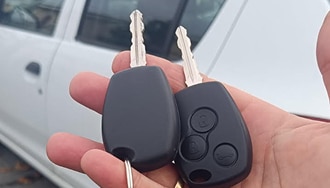 Clés de Voiture Renault : Télécommande et Clé Vierge Main tenant deux clés de voiture Renault, une clé à télécommande noire à trois boutons et une clé de remplacement vierge, devant une voiture blanche.