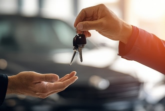 Remise des clés de voiture : transaction et propriété Mains échangeant des clés de voiture neuve ou louée devant un véhicule flou, symbolisant la livraison ou la transaction automobile.