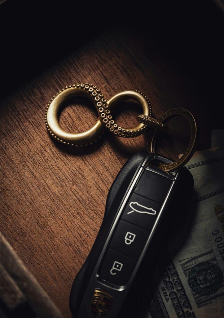 Porte-clés Poulpe Laiton et Clé Porsche de Luxe Sombre Clé Porsche noire et porte-clés infini en laiton sculpté de tentacules. Gravure « GET BUSY DYING », posé sur bois sombre avec billets.